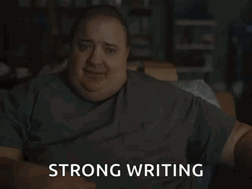 A Man In A Grey Shirt Is Sitting Down And Says Strong Writing GIF