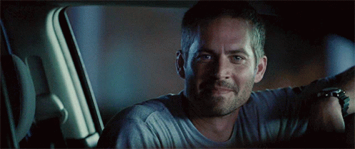 A Man In A Grey Shirt Is Smiling In A Car GIF