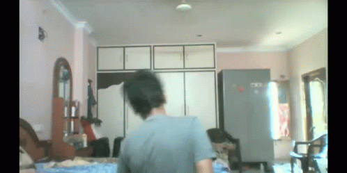 A Man In A Grey Shirt Is Standing In A Room GIF