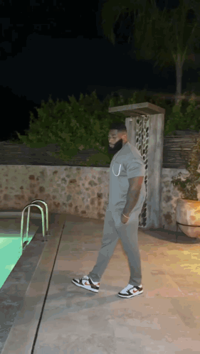 A Man In A Grey Shirt Is Walking By A Swimming Pool At Night . GIF