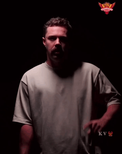 A Man In A Grey Shirt Stands In Front Of A Sign That Says Play With Fire GIF