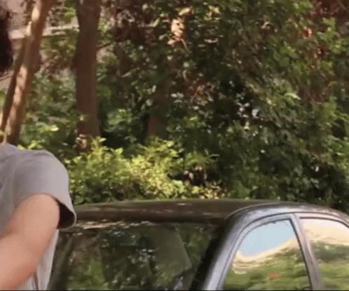 A Man In A Grey Shirt Stands Next To A Black Car GIF