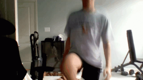 A Man In A Grey Shirt That Says Ny On It Is Standing In A Room GIF