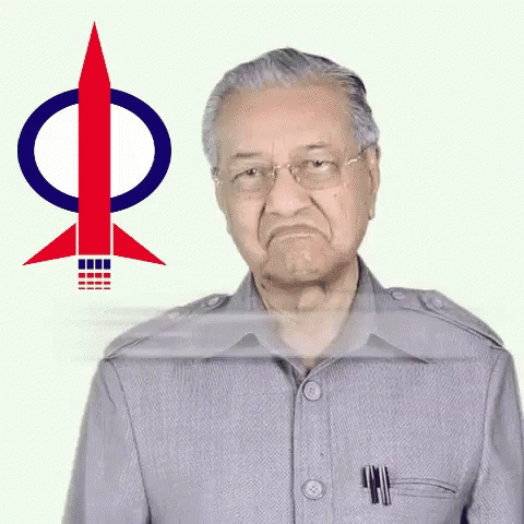 A Man In A Grey Suit Is Standing In Front Of A Rocket With The Letter P On It GIF