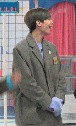 A Man In A Grey Suit Stands In Front Of A Sign That Says ' Eolizh ' On It GIF