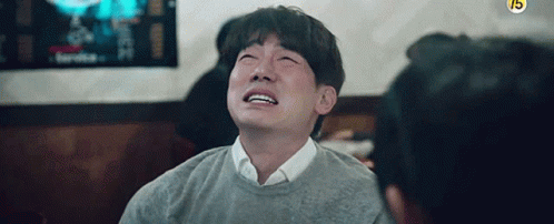 A Man In A Grey Sweater Is Crying While Sitting At A Table . GIF