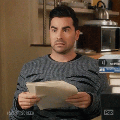 A Man In A Grey Sweater Is Holding A Piece Of Paper In Front Of A Pop Box GIF