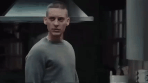 A Man In A Grey Sweater Is Standing In Front Of A Kitchen Hood GIF