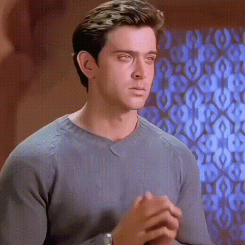 A Man In A Grey Sweater Looks At The Camera With His Eyes Closed GIF