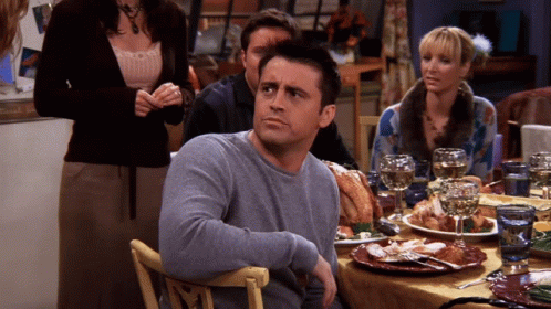 A Man In A Grey Sweater Sits At A Table With Plates Of Food GIF