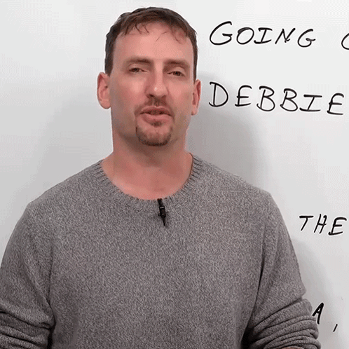 A Man In A Grey Sweater Stands In Front Of A White Board That Says Going Debbie The A GIF