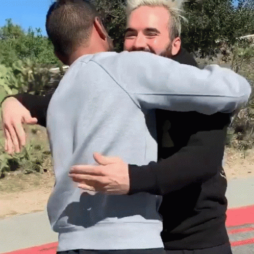 A Man In A Grey Sweatshirt Is Hugging Another Man In A Black Hoodie GIF