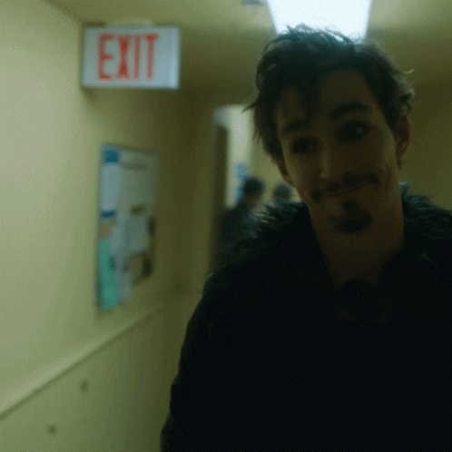 A Man In A Hallway With An Exit Sign Above Him GIF