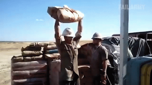 A Man In A Hard Hat Is Carrying A Bag Over His Head GIF