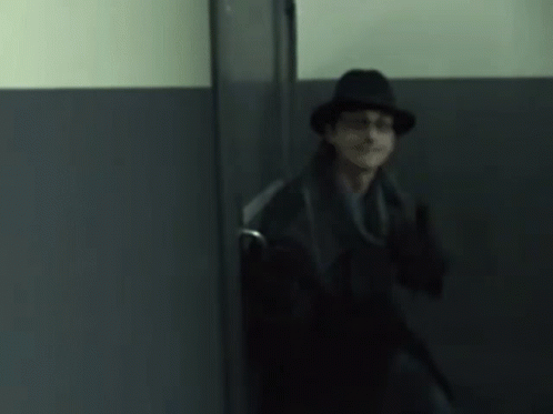 A Man In A Hat And Coat Is Standing In A Doorway GIF