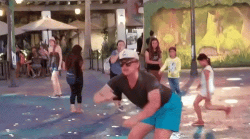A Man In A Hat And Sunglasses Is Dancing In A Water Fountain . GIF