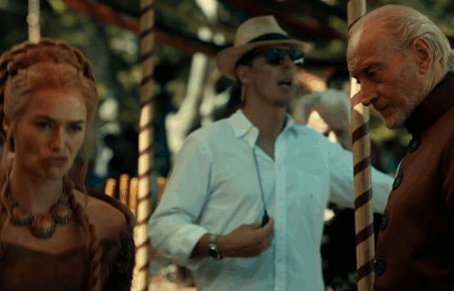 A Man In A Hat And Sunglasses Stands Next To A Woman GIF
