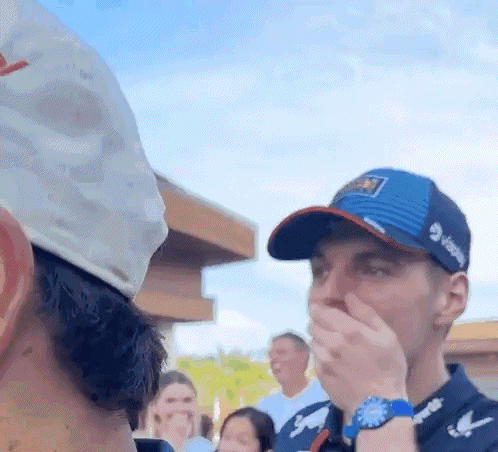 A Man In A Hat Is Covering His Mouth With His Hand While Another Man Looks On . GIF