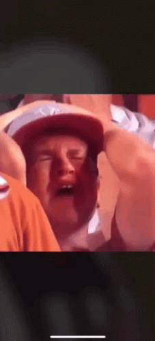 A Man In A Hat Is Crying While Sitting In A Crowd Of People . GIF
