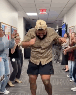 A Man In A Hat Is Dancing In A Hallway With A Group Of People . GIF