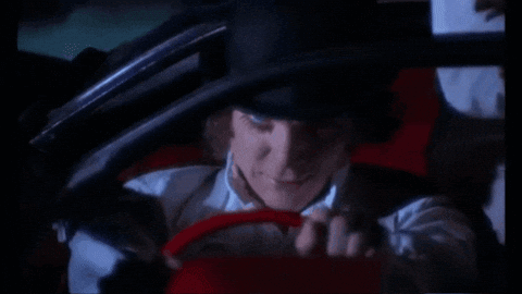 A Man In A Hat Is Driving A Red Car GIF