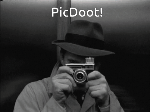 A Man In A Hat Is Holding A Camera In Front Of His Face With The Words Picdoot Below Him GIF