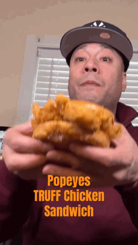 A Man In A Hat Is Holding A Popeye 'S Truffle Chicken Sandwich GIF