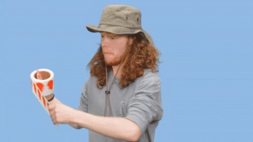 A Man In A Hat Is Holding A Roll Of Tape That Says Labels Are Stickers On It GIF