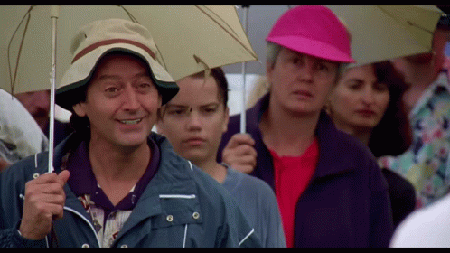 A Man In A Hat Is Holding An Umbrella In A Crowd GIF