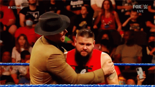 a man in a hat is hugging another man in a red shirt in a wrestling ring