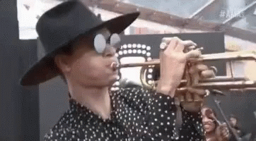A Man In A Hat Is Playing A Trumpet . GIF