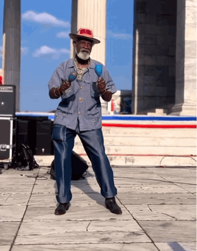 A Man In A Hat Is Playing Maracas On A Stage GIF
