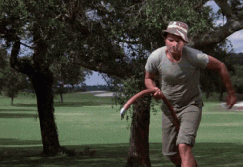 A Man In A Hat Is Running On A Golf Course With A Frisbee In His Hand GIF