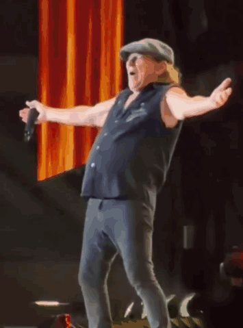 A Man In A Hat Is Singing Into A Microphone With His Arms Outstretched GIF