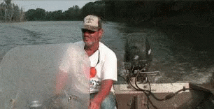 A Man In A Hat Is Sitting In A Boat On A Lake GIF
