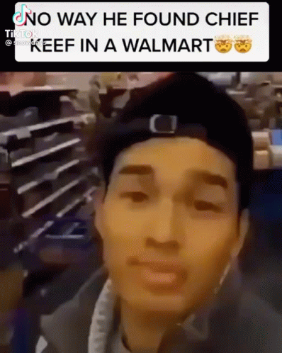 A Man In A Hat Is Standing In A Walmart And Looking At The Camera . GIF