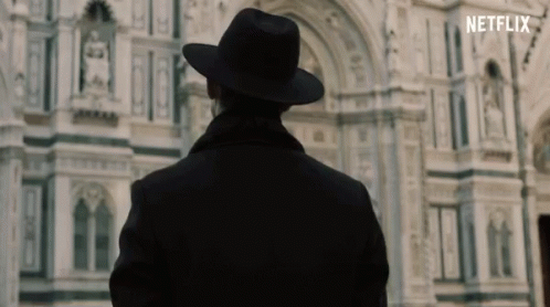 A Man In A Hat Is Standing In Front Of A Building That Says Netflix On The Bottom GIF