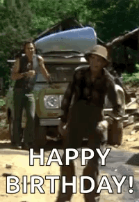 A Man In A Hat Is Standing In Front Of A Car And Says `` Happy Birthday '' . GIF