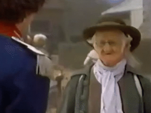 A Man In A Hat Is Talking To Another Man In A Blue Jacket . GIF