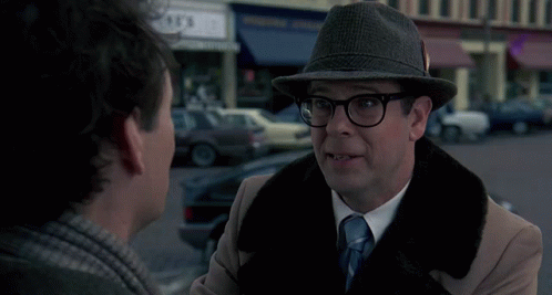 A Man In A Hat Is Talking To Another Man With The Word Bing Behind Him GIF