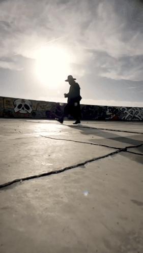 a man in a hat is walking in front of a wall with skulls on it