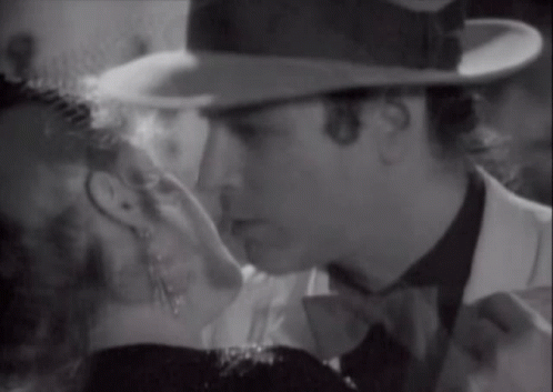 A Man In A Hat Kisses A Woman In A Black And White Photo GIF