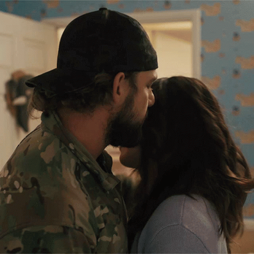 A Man In A Hat Kisses A Woman In A Blue Shirt GIF