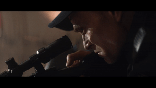 A Man In A Hat Looks Through A Telescope At Something GIF