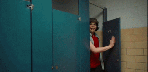 A Man In A Hat Stands In A Bathroom Stall GIF