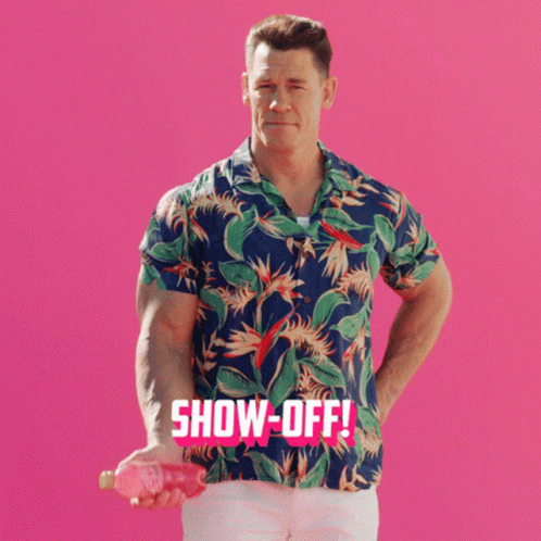 A Man In A Hawaiian Shirt Holds A Pink Object In Front Of A Pink Background That Says Show-Off GIF