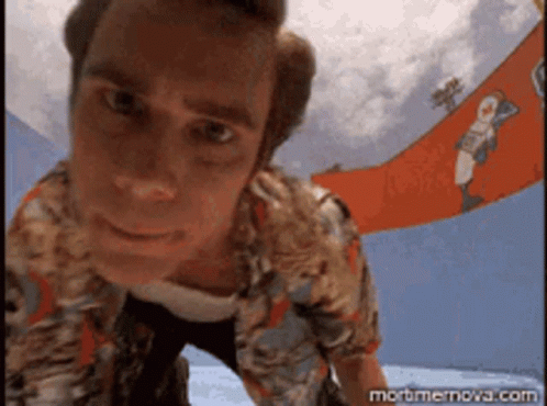 A Man In A Hawaiian Shirt Is Looking Down At The Camera With A Banner In The Background That Says Mortmernova.com GIF