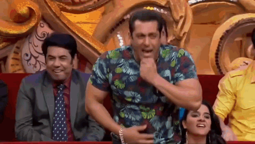 A Man In A Hawaiian Shirt Is Sitting In A Theatre With Other People And Making A Funny Face . GIF
