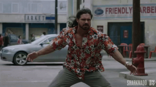A Man In A Hawaiian Shirt Is Standing In Front Of A Fire Hydrant On A City Street . GIF