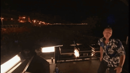 A Man In A Hawaiian Shirt Is Standing In Front Of A Stage At Night GIF